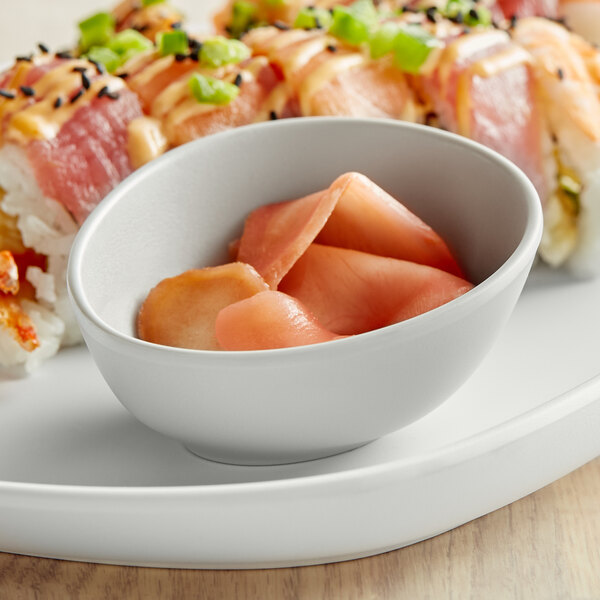 A plate of sushi with a light gray Riverstone ramekin of sauce on a table.