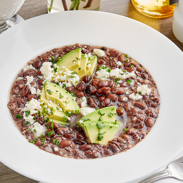 A bowl of Goya black beans with avocado on a white table.