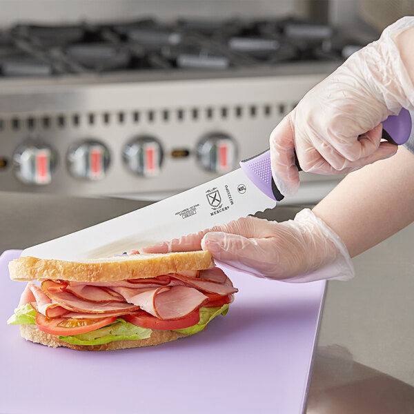 A person using a Mercer Culinary Millennia Colors bread knife to cut a sandwich on a counter.