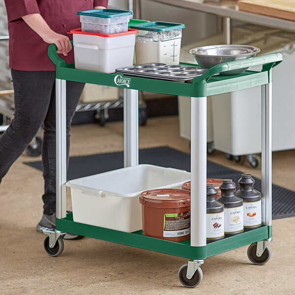 A woman using a green and white Choice utility cart to transport food containers.