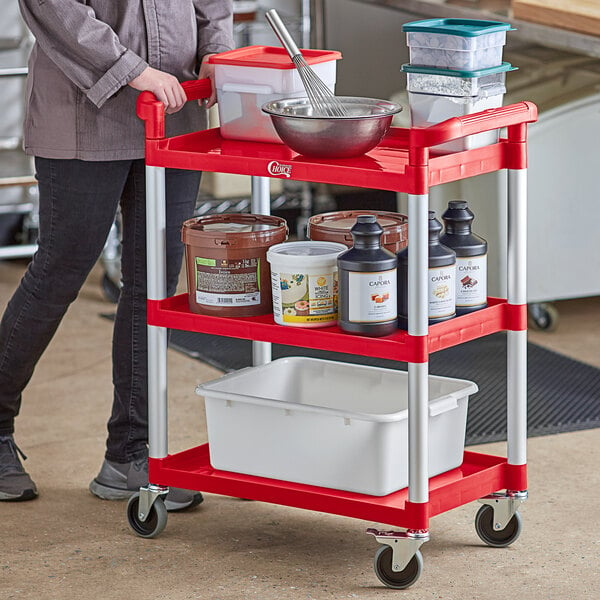 A woman standing next to a red Choice utility cart with white containers on it.