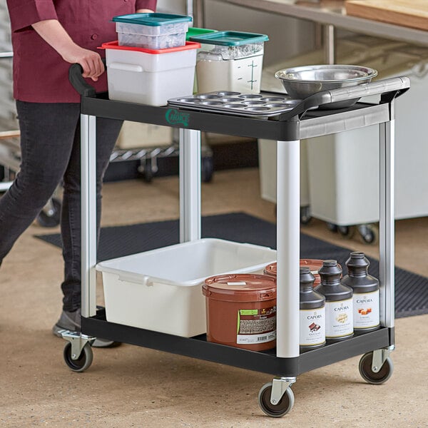 A woman pushing a Choice Black utility cart with containers on it.