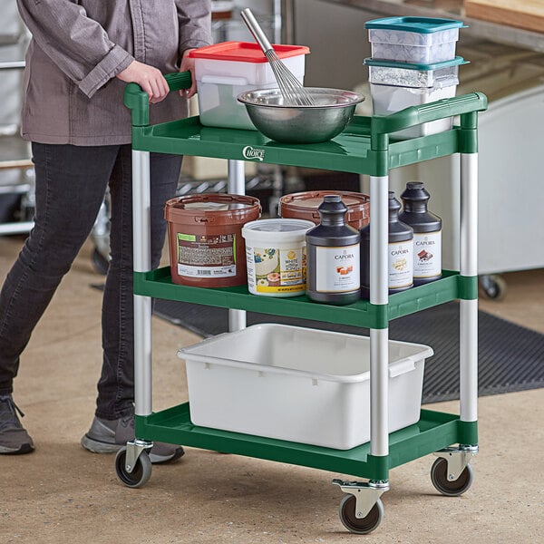 A woman using a green Choice utility cart with white containers on the shelves.