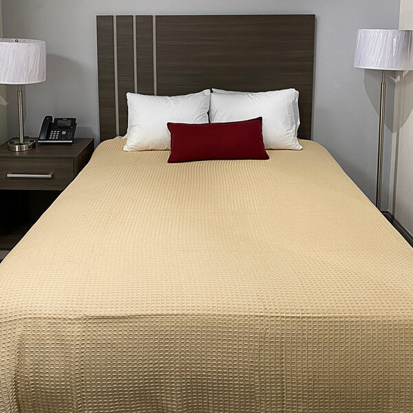 A king size bed made up with a tan Oxford Jaipur thermal honeycomb hotel blanket and pillows.