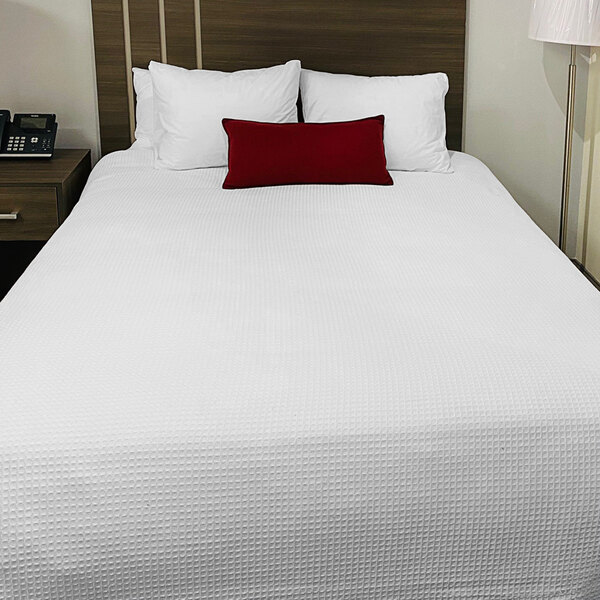 A bed with a white Oxford Jaipur thermal honeycomb blanket and a red pillow.