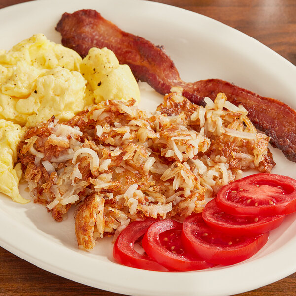 A plate of food with bacon, eggs, and Idahoan Shreds Fresh Cut Hash Browns on a table.