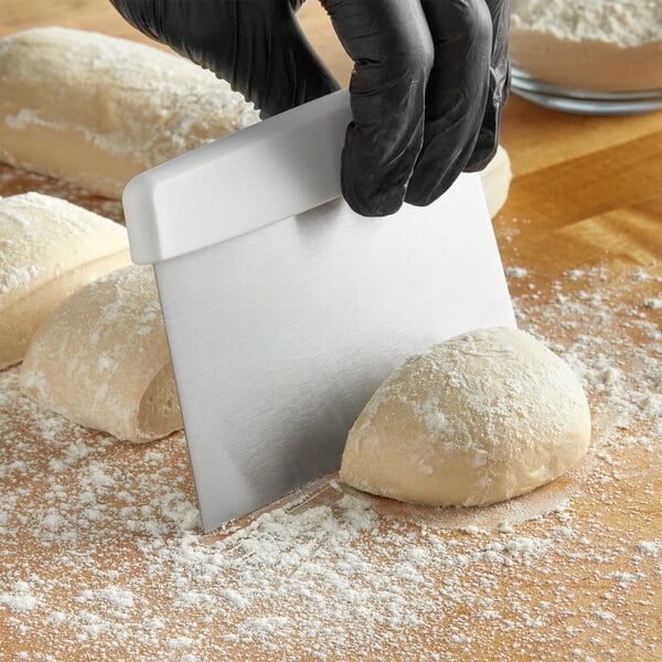 A person in black gloves using a Choice stainless steel dough cutter to cut white floured dough.