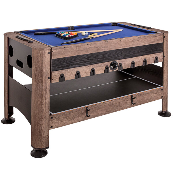 A Triumph 4-in-1 swivel game table with pool sticks on top of a blue felt pool table.