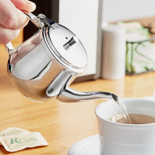 A person pouring water into a Choice stainless steel teapot.