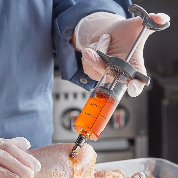 A hand in gloves using an Outset marinade injector to add liquid to a piece of meat.
