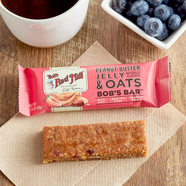 A Bob's Red Mill Peanut Butter Jelly & Oats bar next to a cup of coffee.