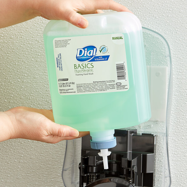 A person holding a Dial Basics hand wash refill bottle over a soap dispenser.