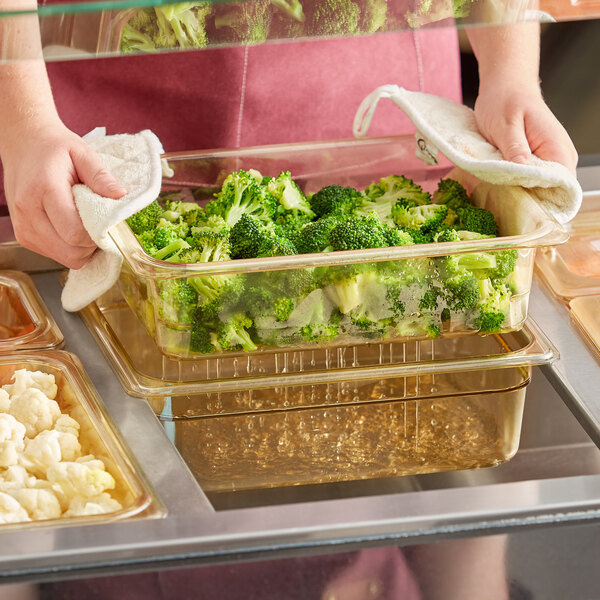 A person using a Cambro H-Pan with a colander to hold broccoli over a tray.