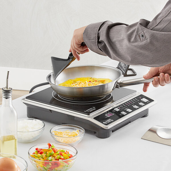 A person using a Global Solutions countertop induction range to cook chopped bell peppers in a pan.