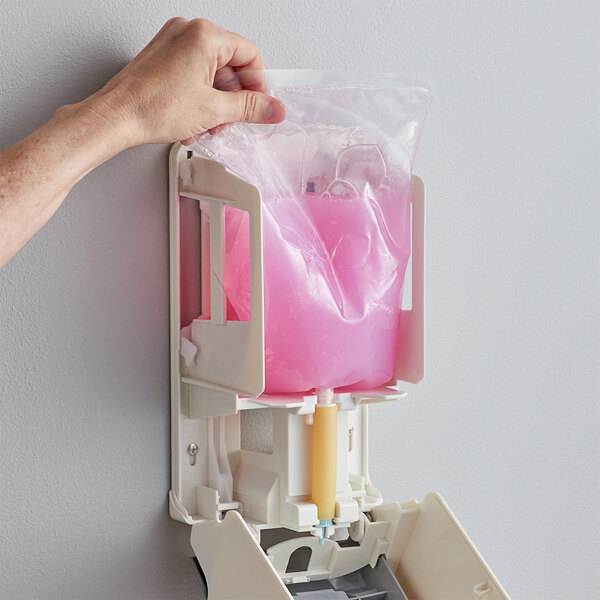A hand refilling a wall-mounted pink Dial liquid hand soap dispenser with pink liquid.