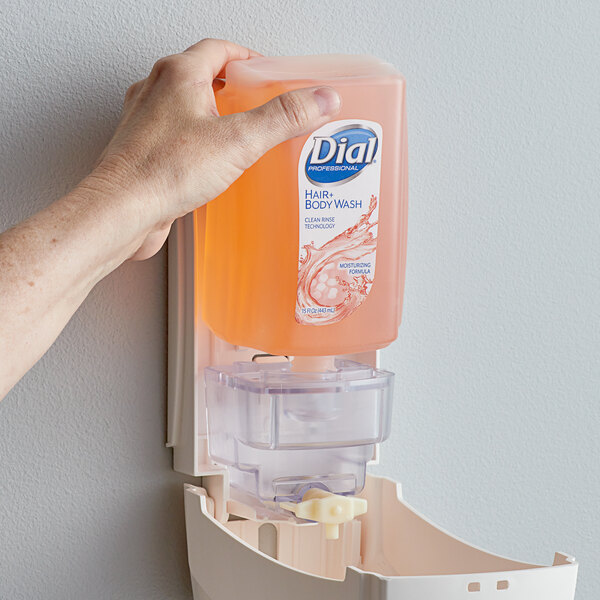 A hand holding a Dial hair and body wash dispenser.