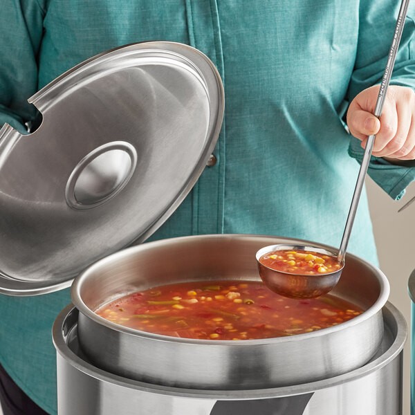 A woman using a Vollrath stainless steel ladle to serve soup from an inset pot.