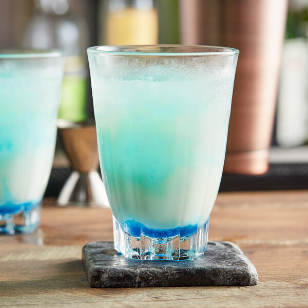 Two Arcoroc Arcadie highball glasses filled with blue drinks on a black surface.