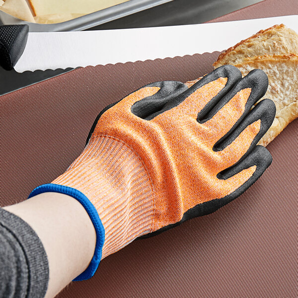A hand wearing orange and white Mercer Culinary Millennia food processing gloves cuts a piece of bread.