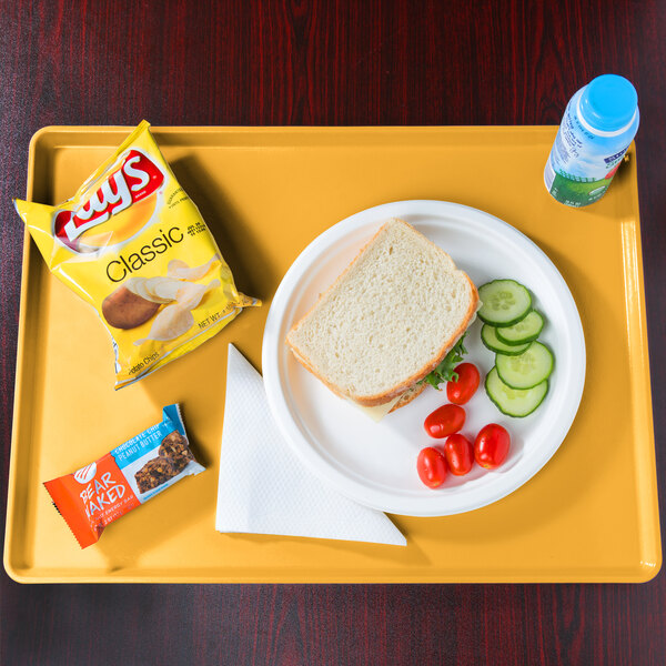A Cambro mustard dietary tray with a sandwich, vegetables, and a bottle of water on it.