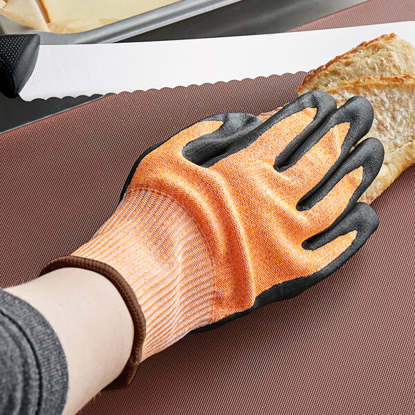 A person wearing a Mercer Culinary Millennia food processing glove cutting bread.