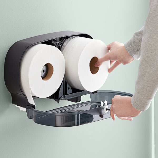 A hand putting Lavex Select 2-ply jumbo toilet paper into a dispenser.