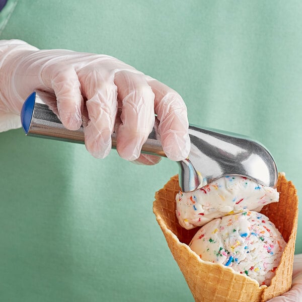 A person using a Choice Aluminum Blue Ice Cream Scoop to add ice cream to a waffle cone.
