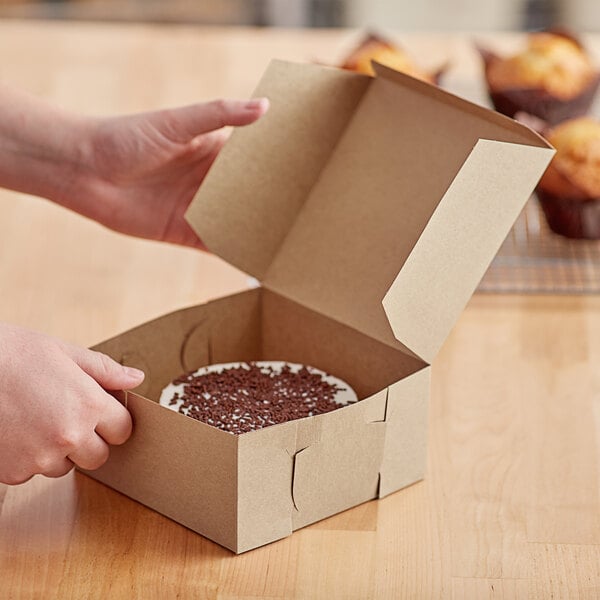 A person opening a Baker's Mark Kraft bakery box with a cake inside.
