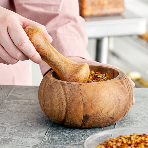 A person using a Fox Run acacia wood mortar and pestle to grind spices.