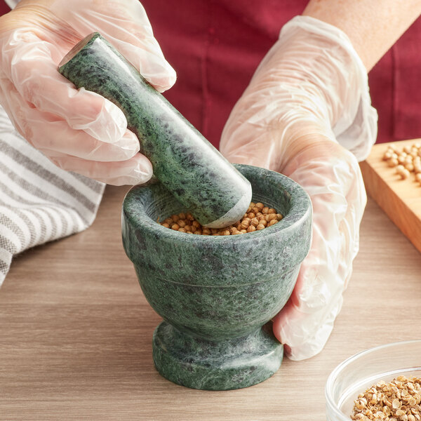 A person grinding nuts in a Fox Run green marble mortar and pestle.