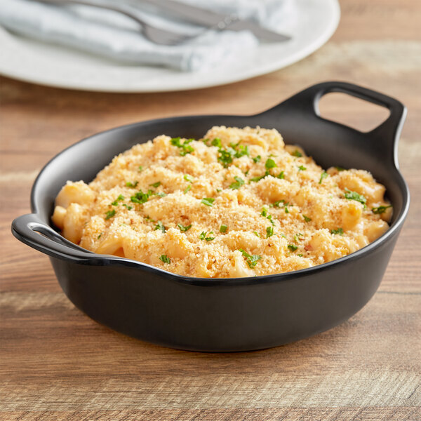 An American Metalcraft black faux cast iron casserole serving dish with macaroni and cheese on a table.