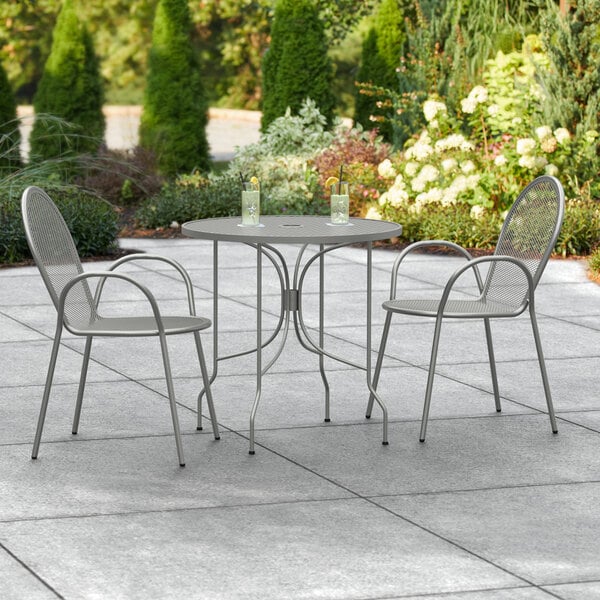 A Lancaster Table & Seating Harbor Gray round outdoor table with two chairs on a patio.