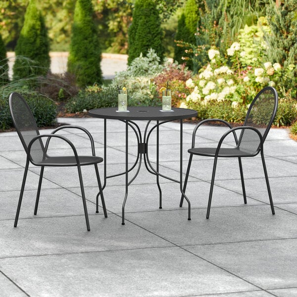 A Lancaster Table & Seating Harbor black outdoor table with two black chairs on a tile patio.