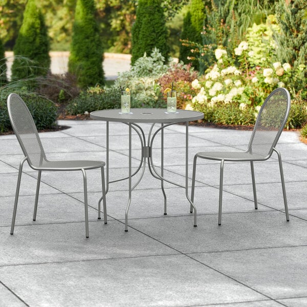 A Lancaster Table & Seating Harbor Gray outdoor table with two chairs on a patio.