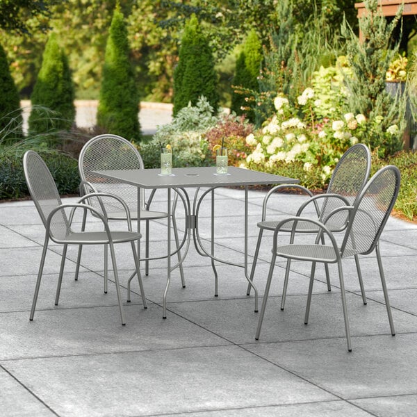 A Lancaster Table & Seating Harbor Gray outdoor patio table with ornate legs and four arm chairs.