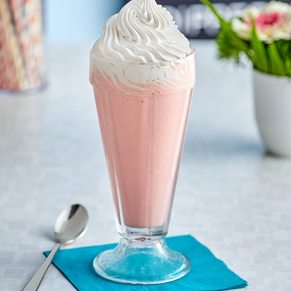 A glass of J. Hungerford Smith strawberry milkshake with whipped cream on a white surface.