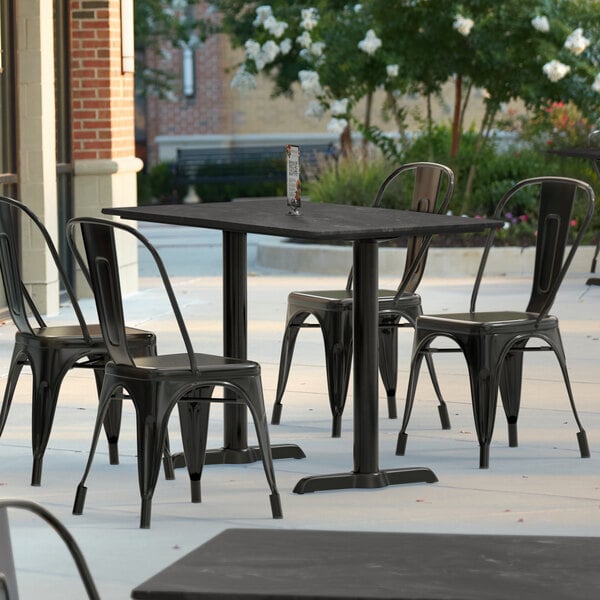 A Lancaster Table & Seating Excalibur rectangular dining table with black metal chairs on an outdoor patio.