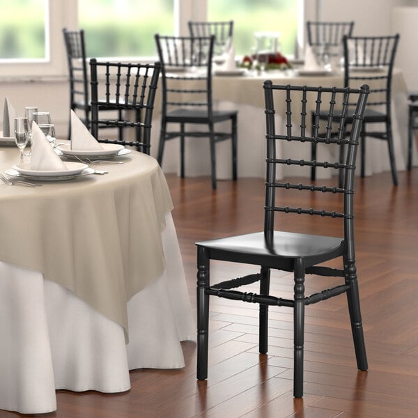 A close-up of a black Lancaster Table & Seating resin Chiavari chair next to a table.