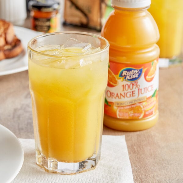 A glass of Ruby Kist Orange Juice with ice on a table next to a bottle of orange juice.
