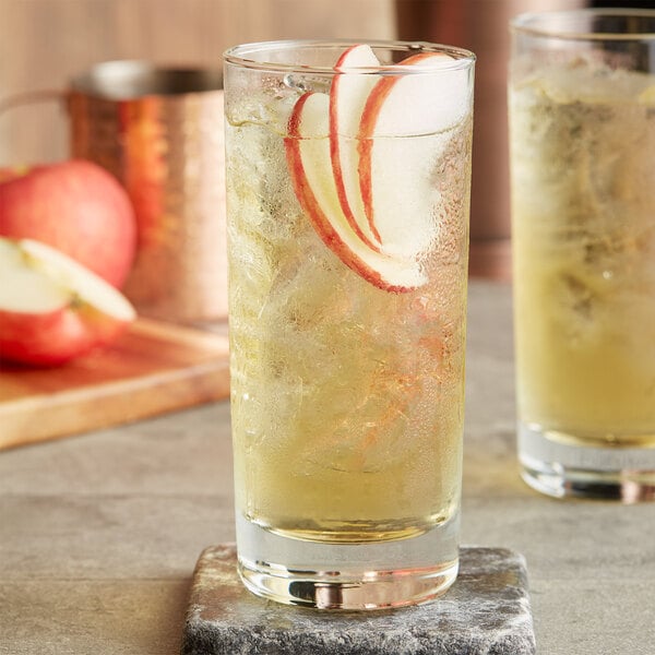 A Ruby Kist glass of apple juice with ice and a slice of apple.