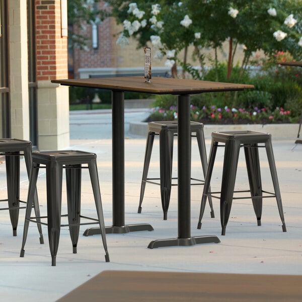 A Lancaster Table & Seating rectangular counter height table with a brown textured surface and metal end plates on an outdoor patio.