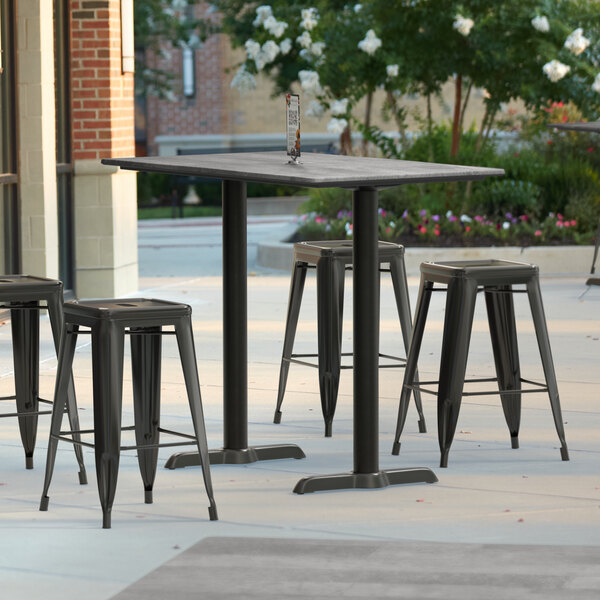 A Lancaster Table & Seating rectangular outdoor table with textured Toscano finish on a patio with two end base plates for stools.