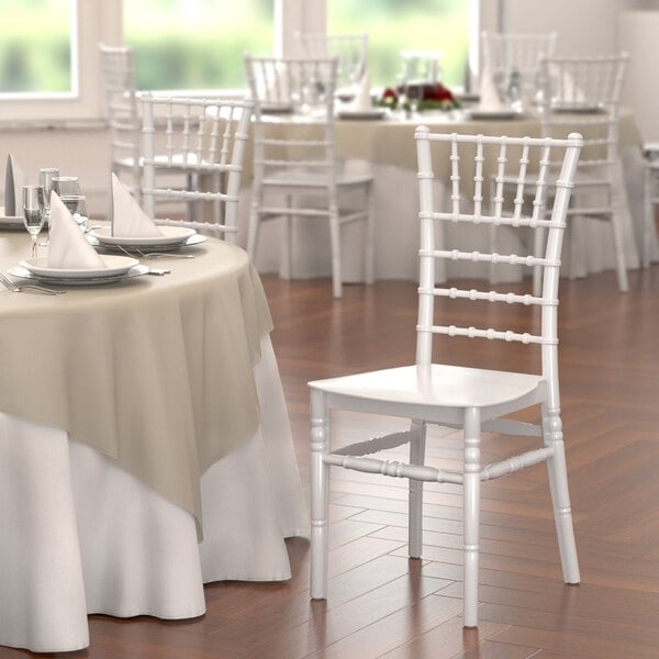 A white Lancaster Table & Seating White Resin Chiavari chair next to a table with plates and napkins.