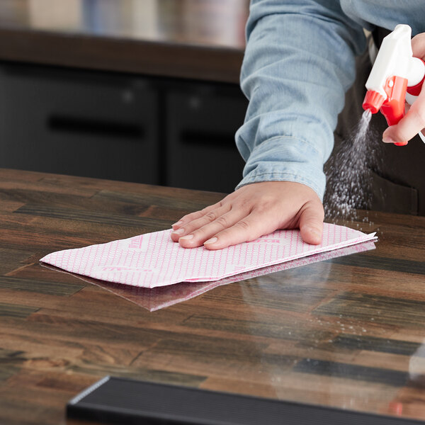 A hand using a red WypAll X70 wiper to clean a table in a professional kitchen.
