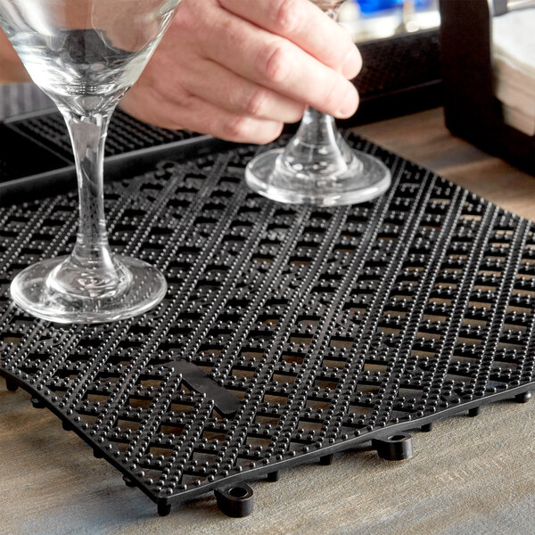 A hand holding a wine glass on a black Tablecraft bar mat.