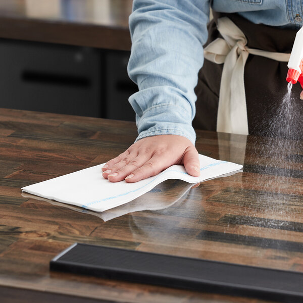 A person cleaning a wooden countertop with a WypAll foodservice wiper.