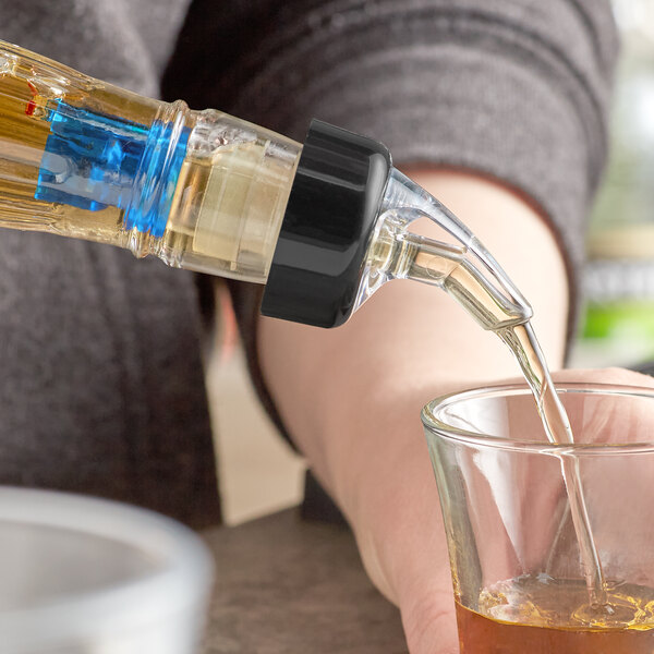 A person using a TableCraft blue tail liquor pourer to pour liquid into a glass.