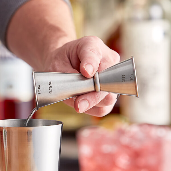 A person using a Tablecraft stainless steel Japanese jigger to pour liquid into a cup.