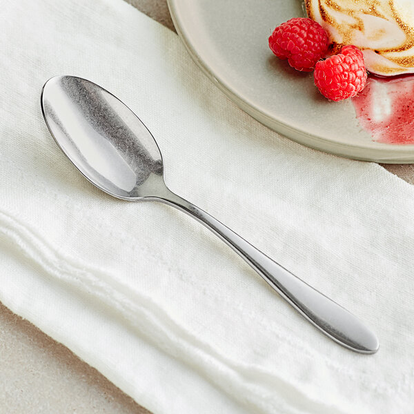 An Acopa Pangea stainless steel teaspoon on a plate of raspberries.