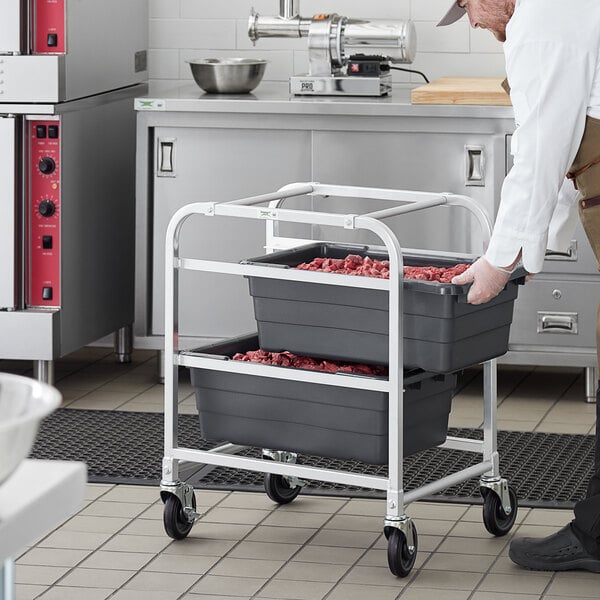 A man in a chef's uniform pushing a Regency aluminum lug rack with gray meat lugs on it.
